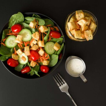 croutons on spinach salad as well as in small jar next to salad bowl, with dressing and fork on table nearby.