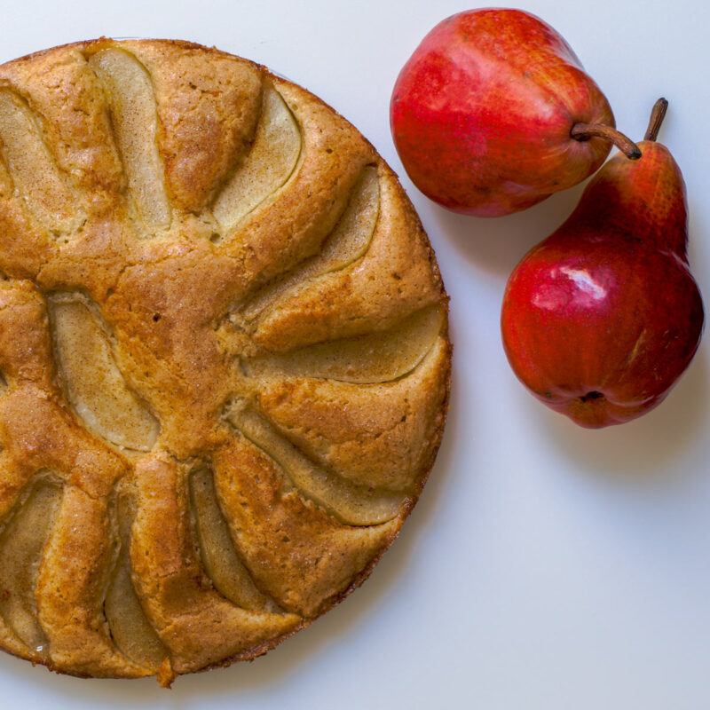 whole pear cake on white board next to two red pears.