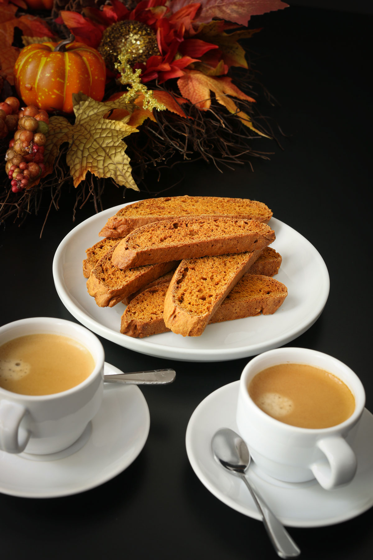 table set with fall decor, a platter of pumpkin biscotti and two demitasse cups of espresso with saucers and spoons.