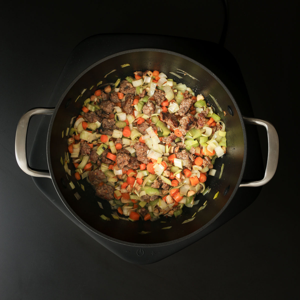 vegetables cooking with sausage in pot.
