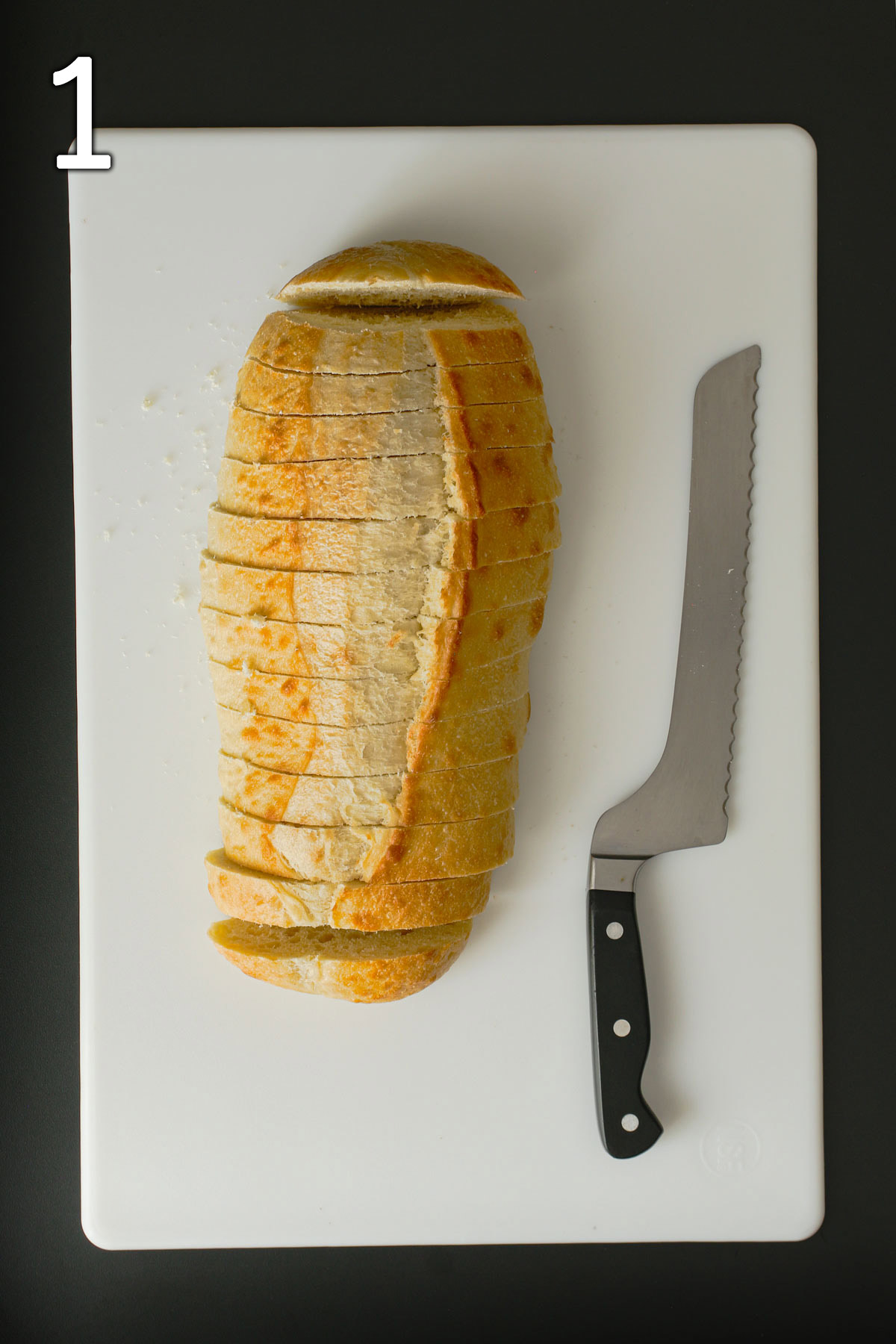 bread loaf cut into slices on white board next to bread knife.