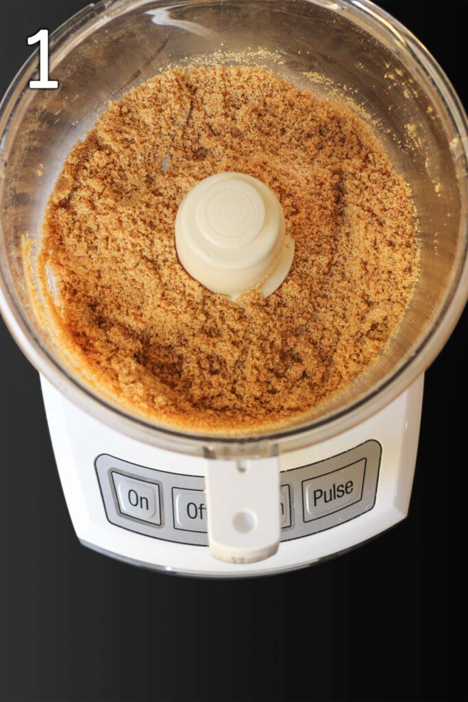graham cracker crumbs in the bowl of a food processor fitted with a metal blade.