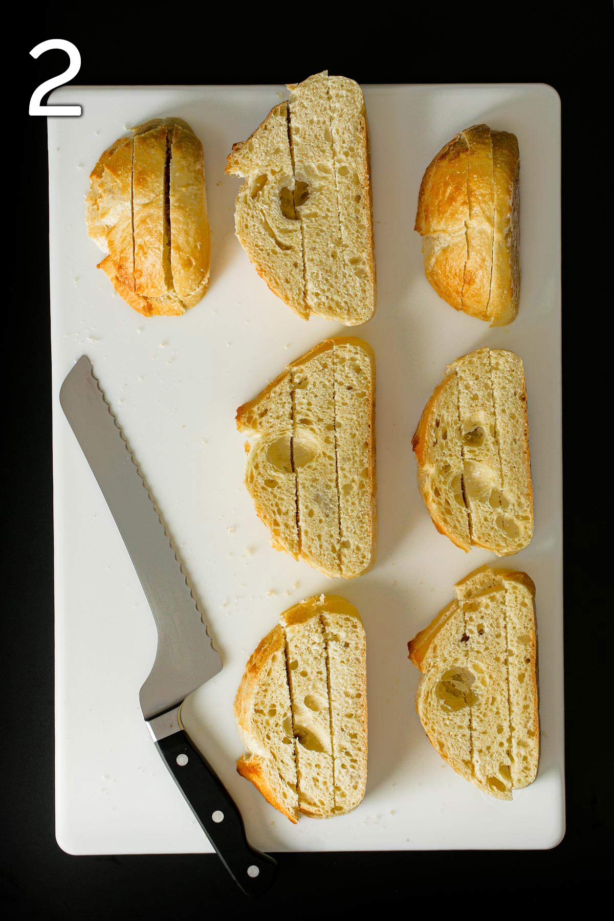 stacked bread slices cut into strips on white board next to bread knife.
