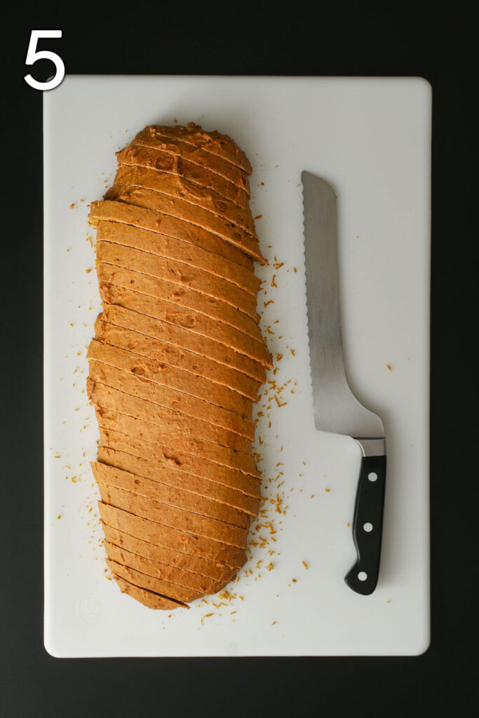 sliced biscotti log on cutting board with serrated bread knife.