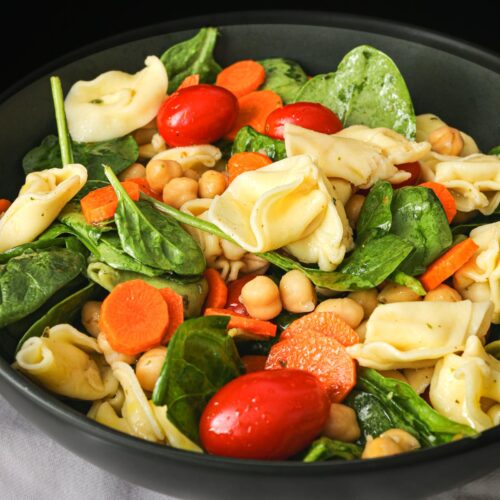 close up of pasta salad with tortellini in black bowl.