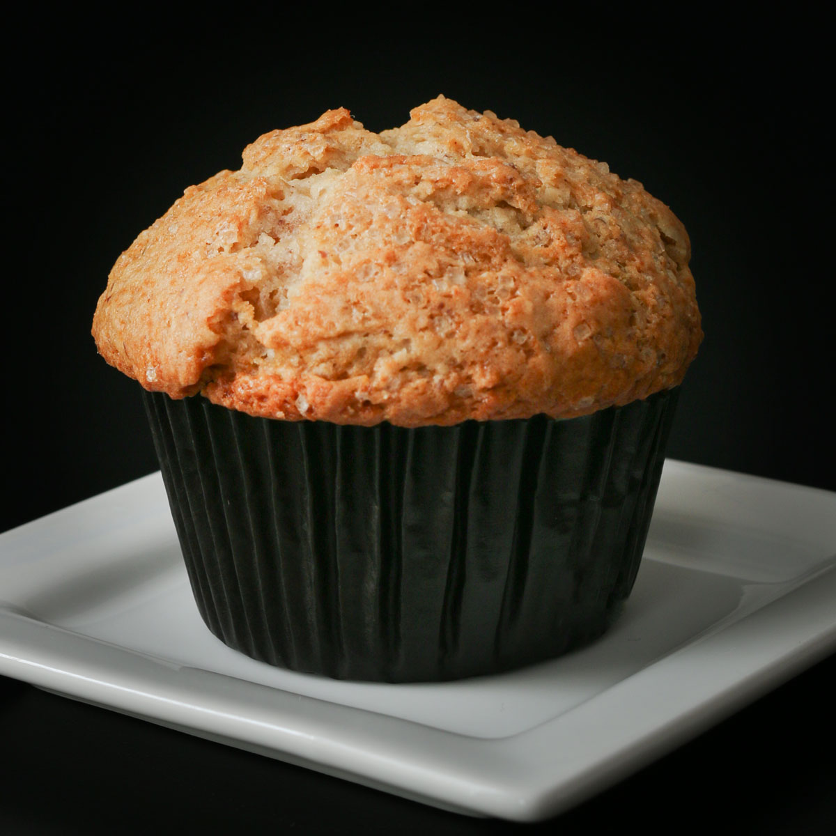 vegan muffin in black muffin paper on white square plate on black table.