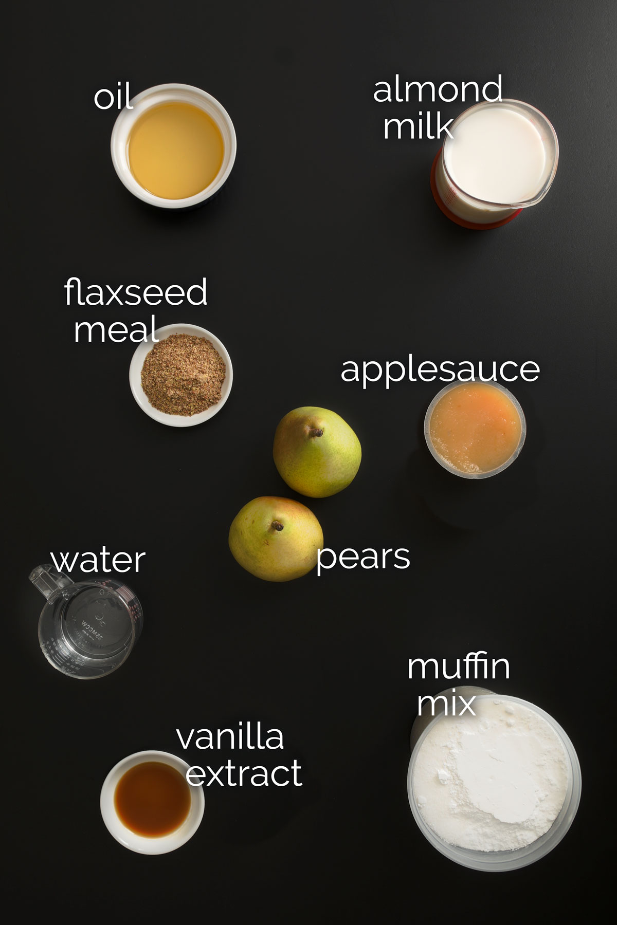 ingredients for vegan muffins measured into dishes and laid out on a black table top.