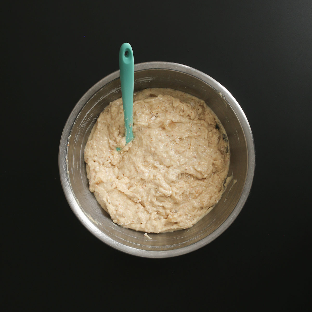 mixed muffin batter in a large mixing bowl with a teal rubber spatula.