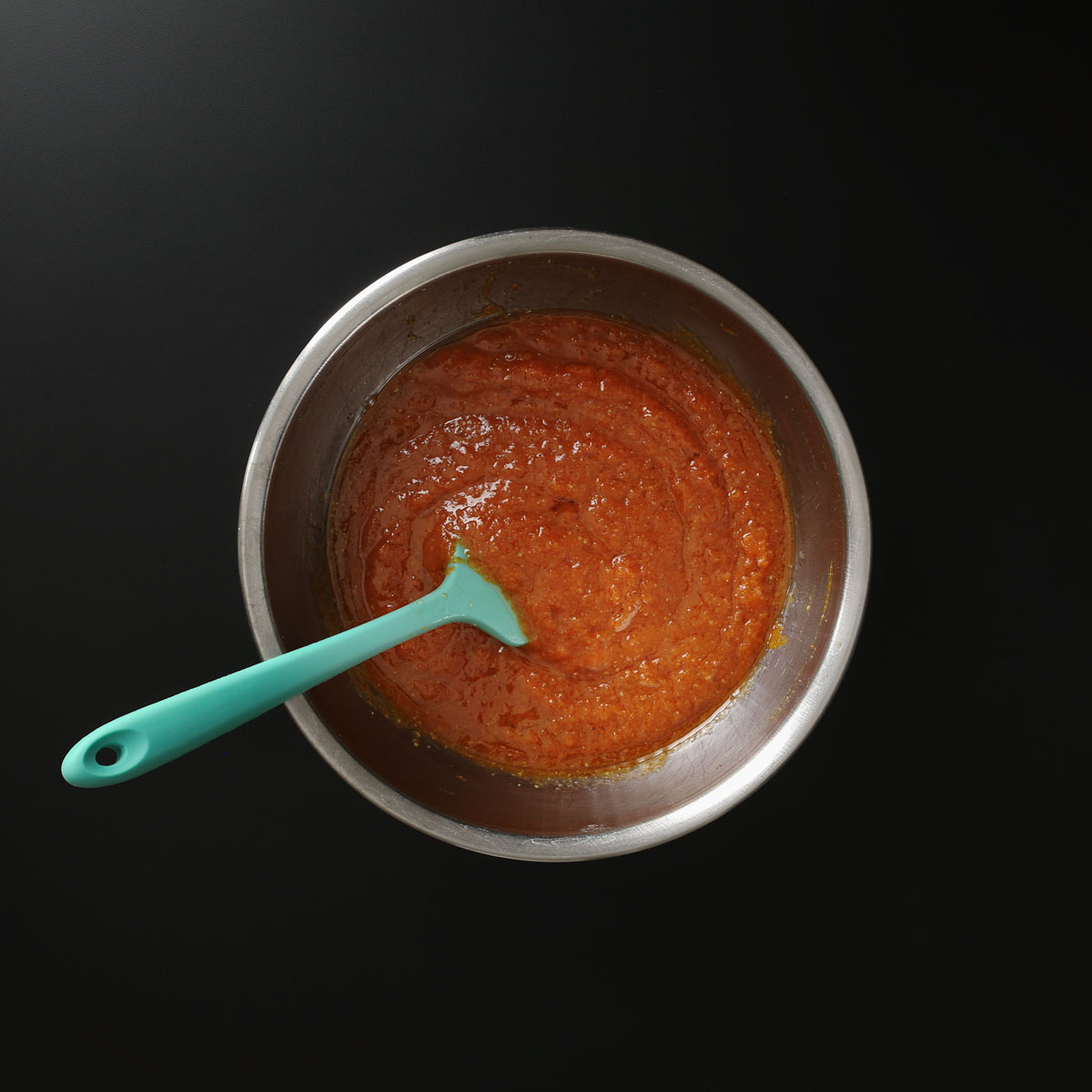 teal spatula immersed in pumpkin mixture in large mixing bowl.