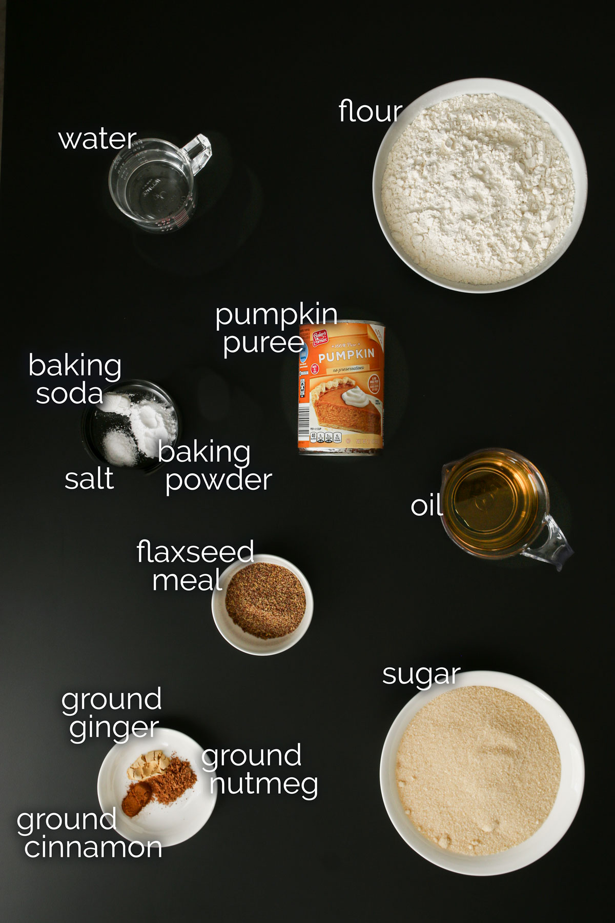 ingredients for vegan pumpkin bread measured into dishes and laid out on a black table top.