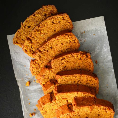 slices of pumpkin bread laid out on parchment paper on black cutting board.