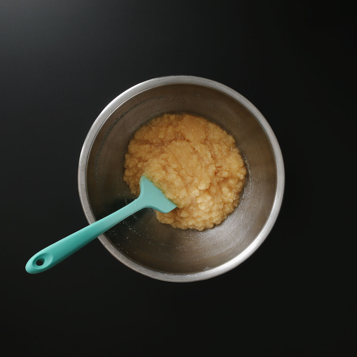 teal rubber spatula immersed in sugar and oil mixture in bowl.
