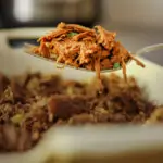 shredded beef scooped up on a fork suspended over a serving dish of the meat near the instant pot.