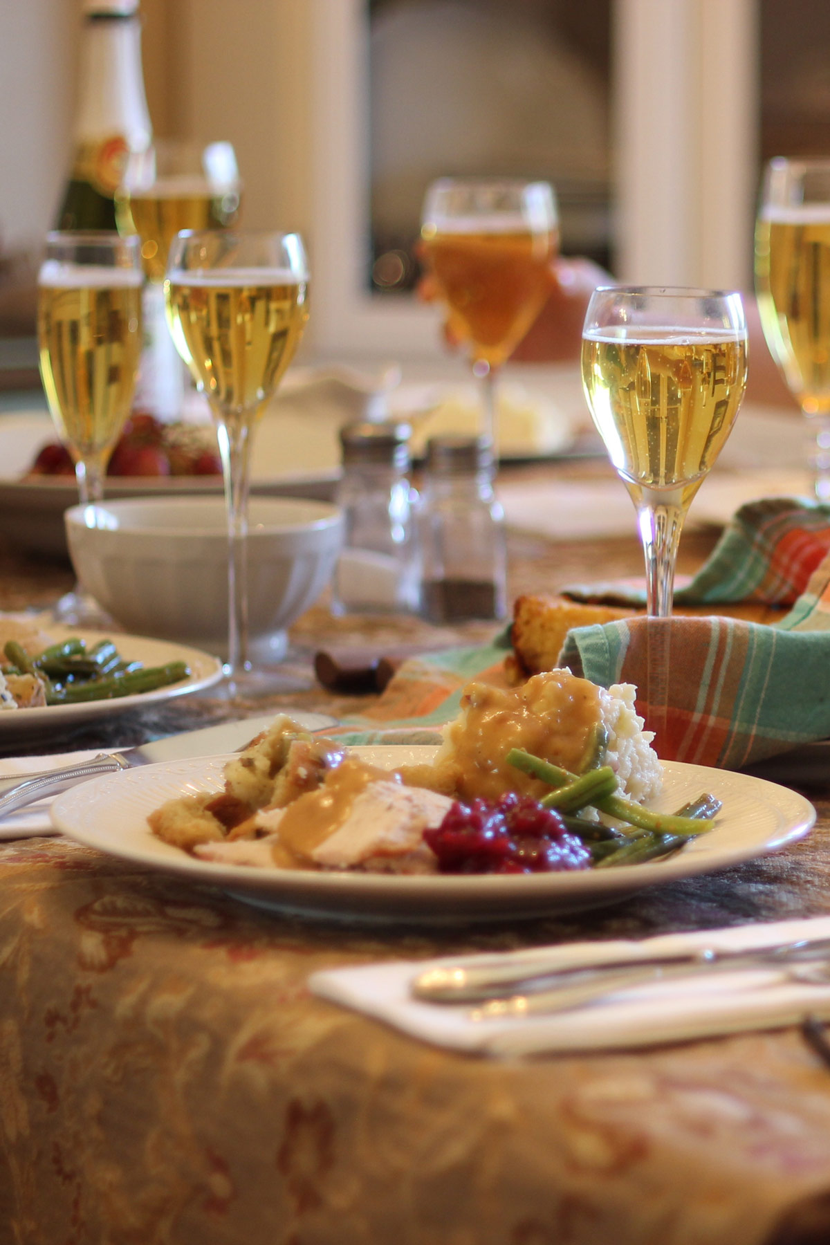 table set with gold tablecloth, full plates of food, and goblets filled with wine or sparkling apple cider.