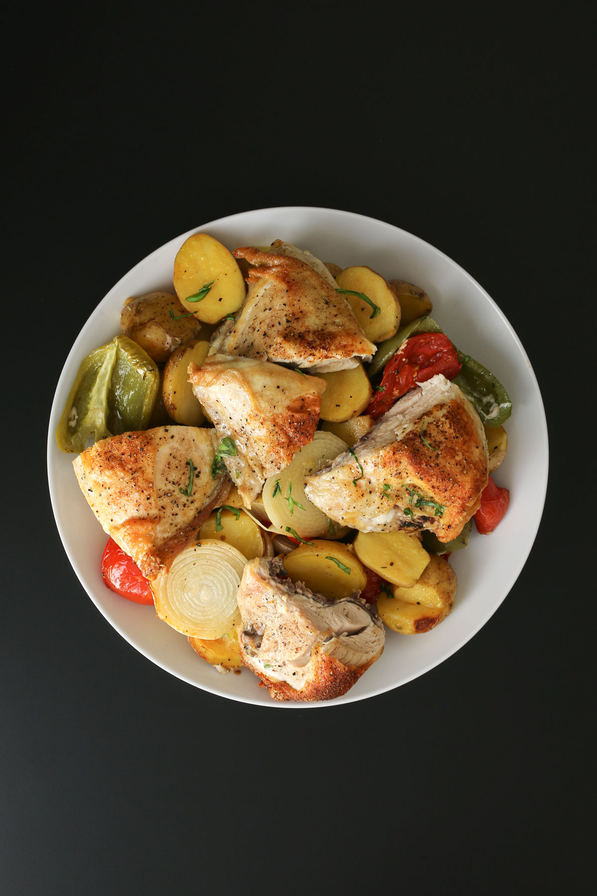 chicken pieces arranged atop a white platter of vegetables on a black table.
