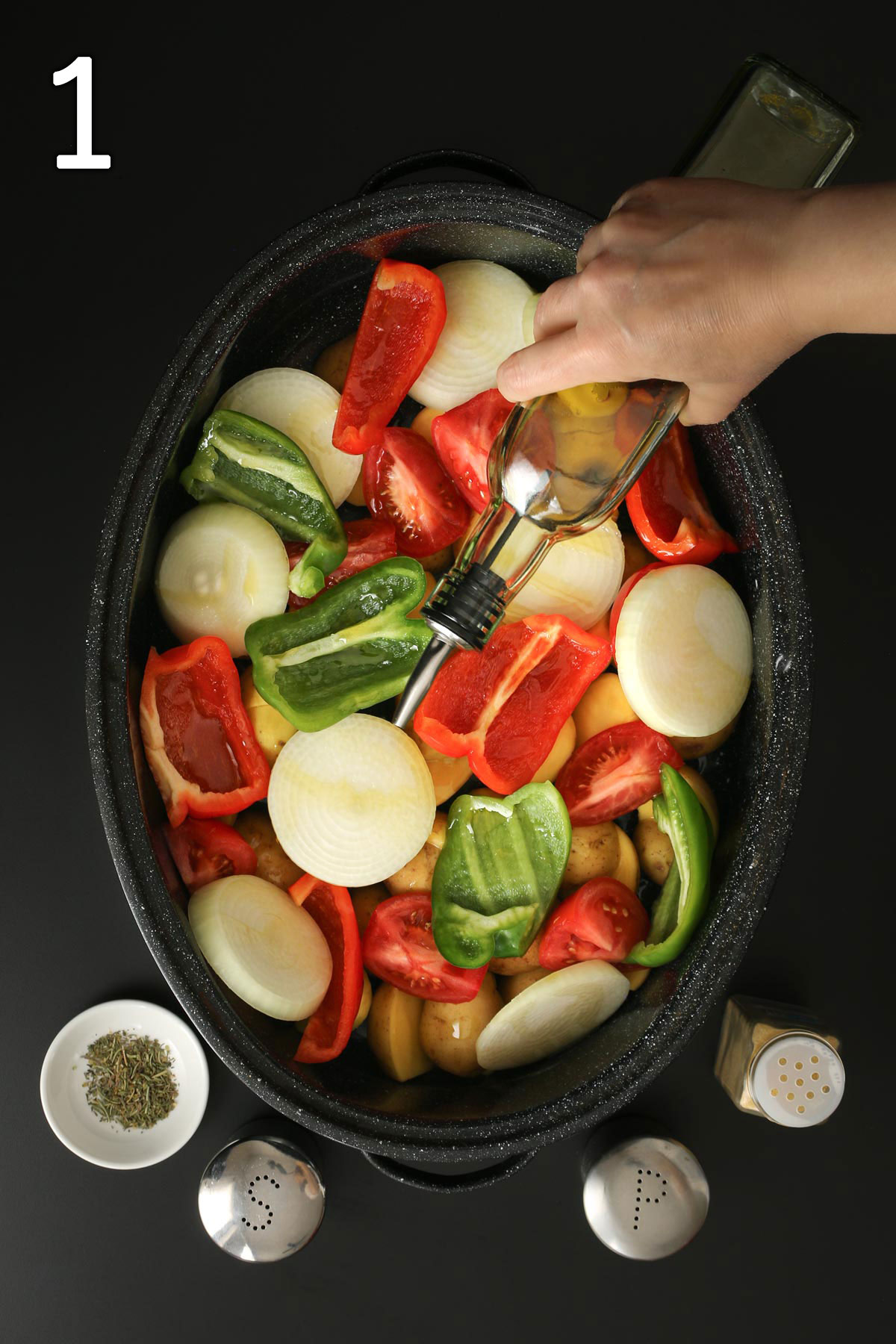 pouring oil over vegetables in large roasting pan on a table with seasonings nearby.