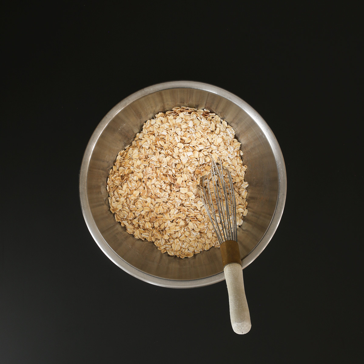 a wire whisk with a wooden handle submerged into the dry ingredients in mixing bowl.