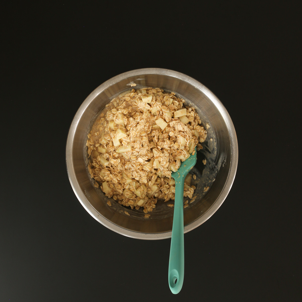 teal rubber spatula submerged in prepared oatmeal batter in mixing bowl on work surface.