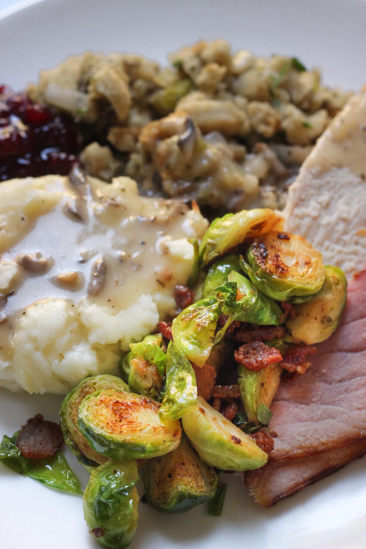 sautéed Brussels sprouts on dinner plate with ham, turkey, stuffing, mashed potatoes and gravy.