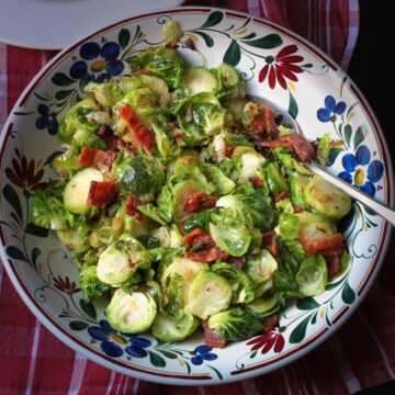 Brussels sprouts and bacon in flowered bowl on red cloth.