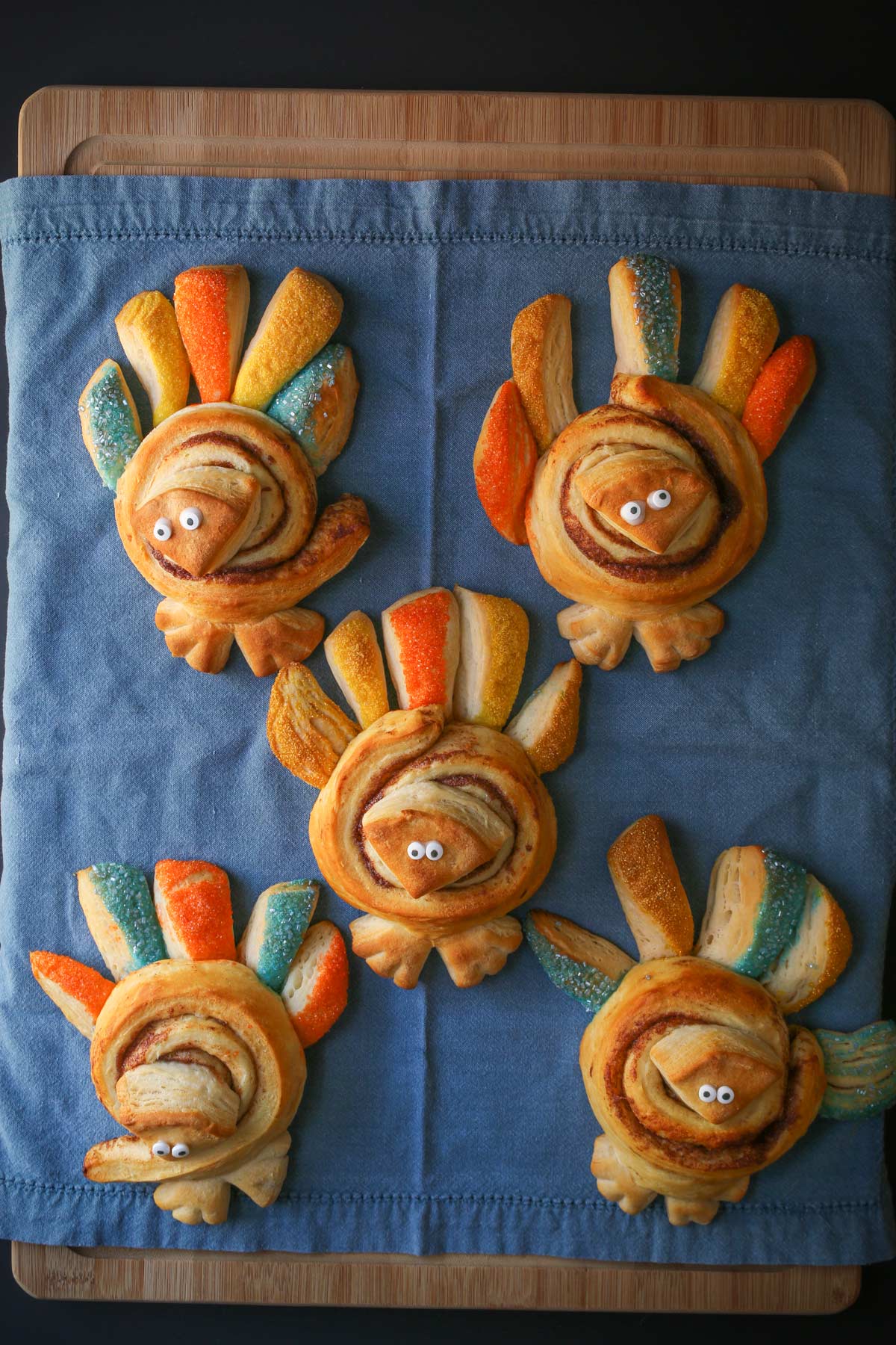 array of five cinnamon roll turkeys on a blue cloth on a wooden board.