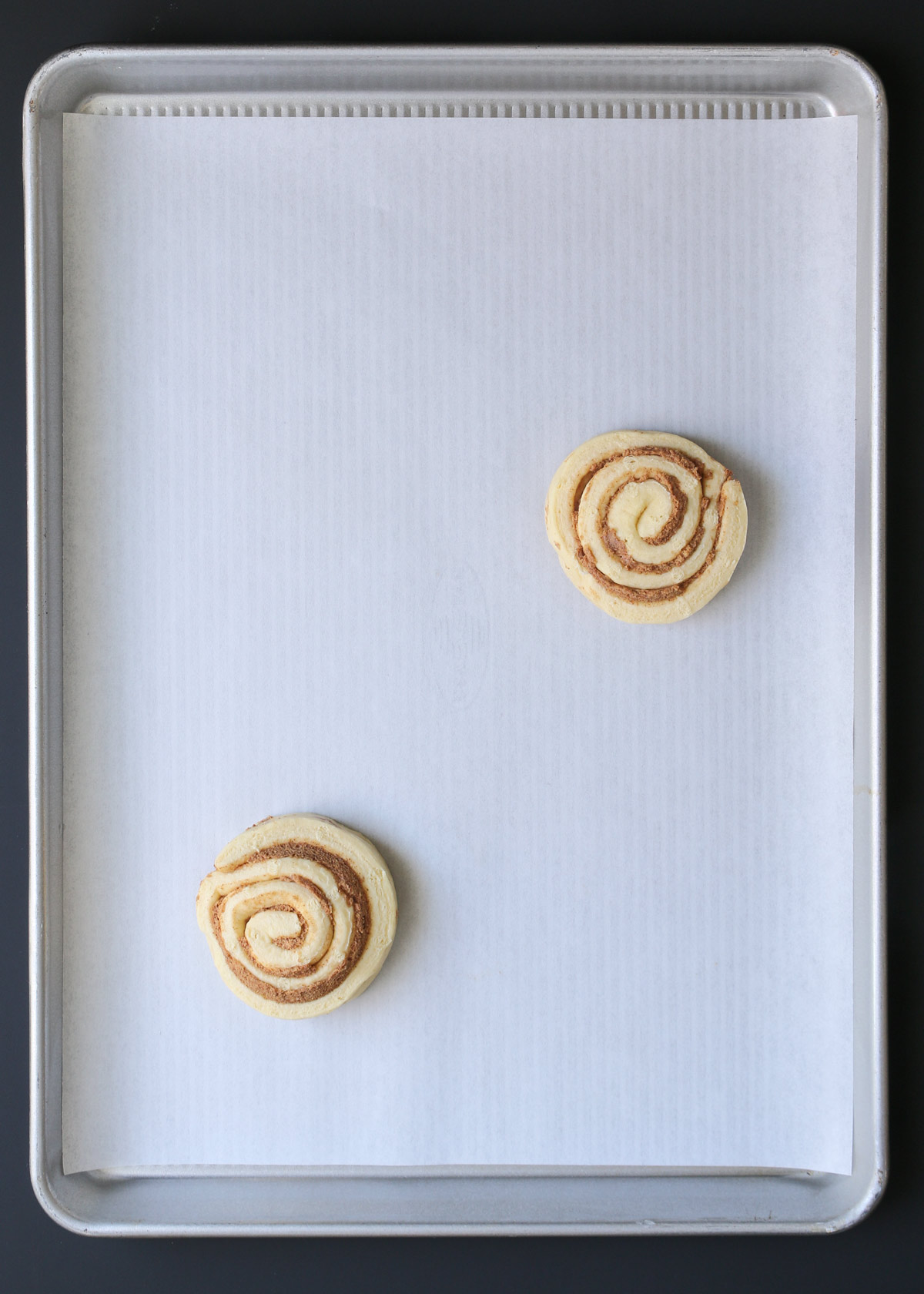 two cinnamon rolls on parchment-lined baking sheet.