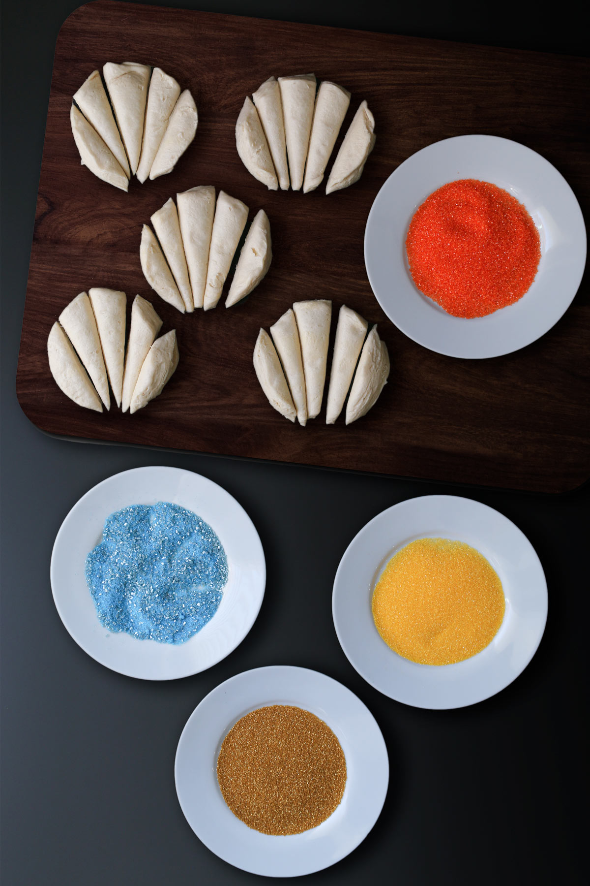 biscuit feathers on cutting board next to dishes of colored sugars.