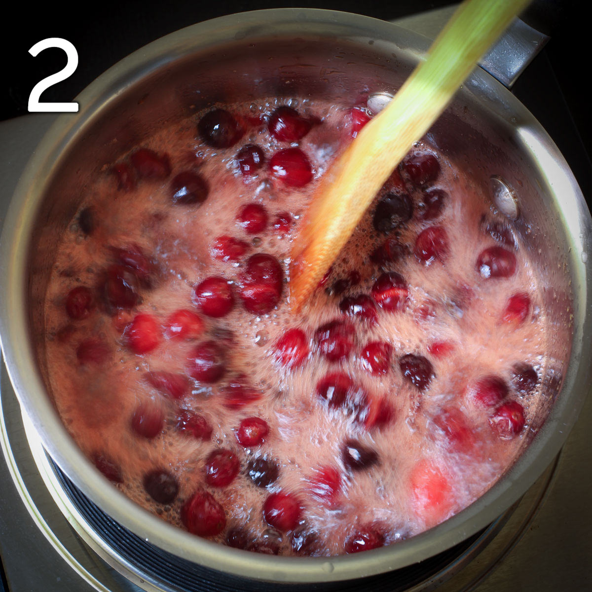 cranberries boiling in pot, stirring with wooden spoon.