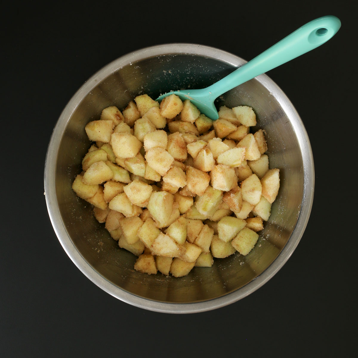 teal spatula immersed in bowl of apple mixture.
