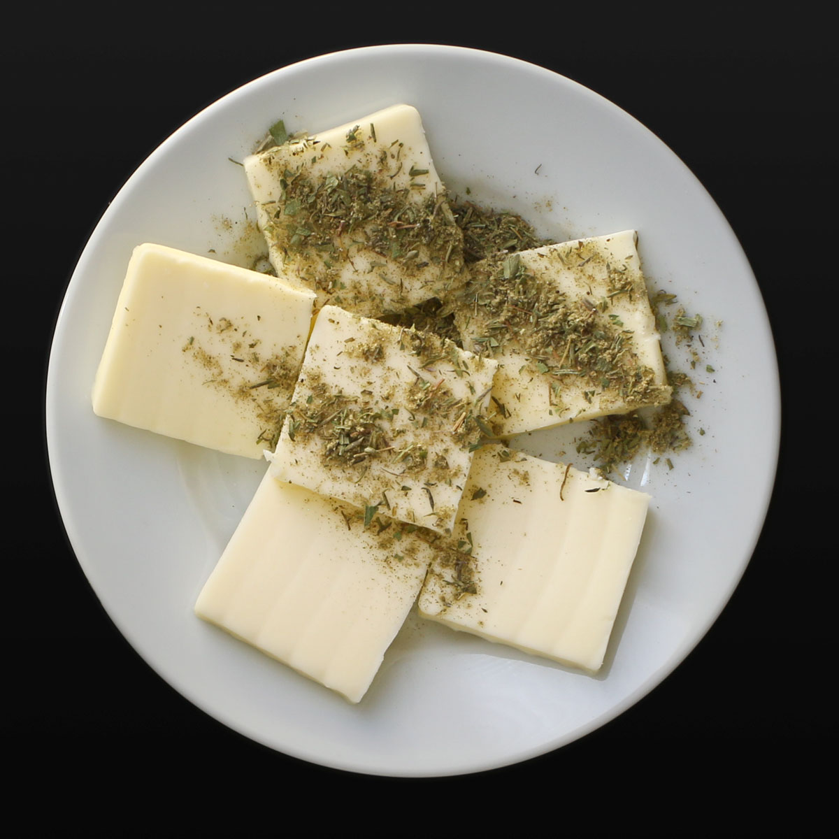 herbs sprinkled over butter pats on a white plate.