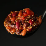 ladleful of quinoa chili in front of a black background.