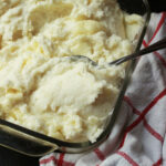 spoon inserted in baking dish full of fluffy make-ahead mashed potatoes.