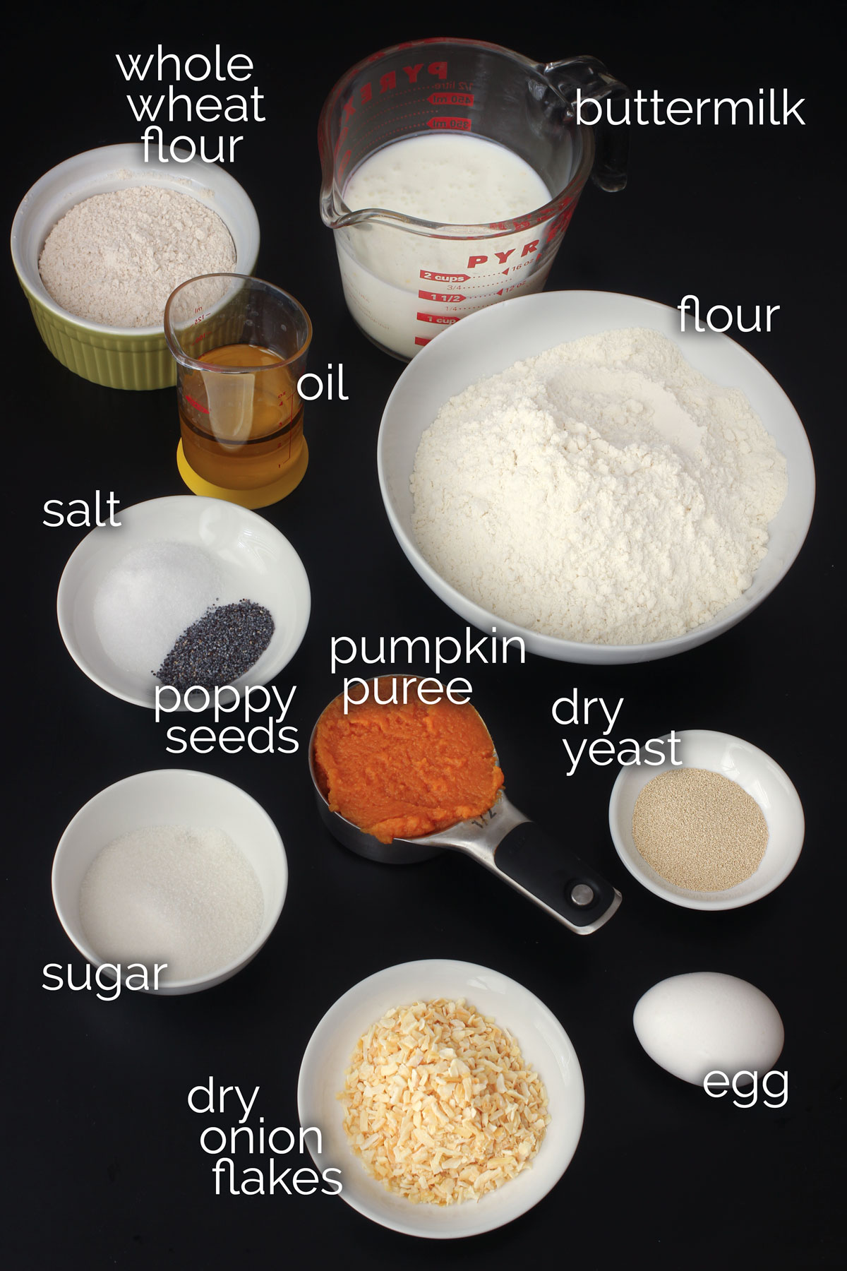 ingredients for pumpkin dinner rolls measured out in dishes on a black table top.