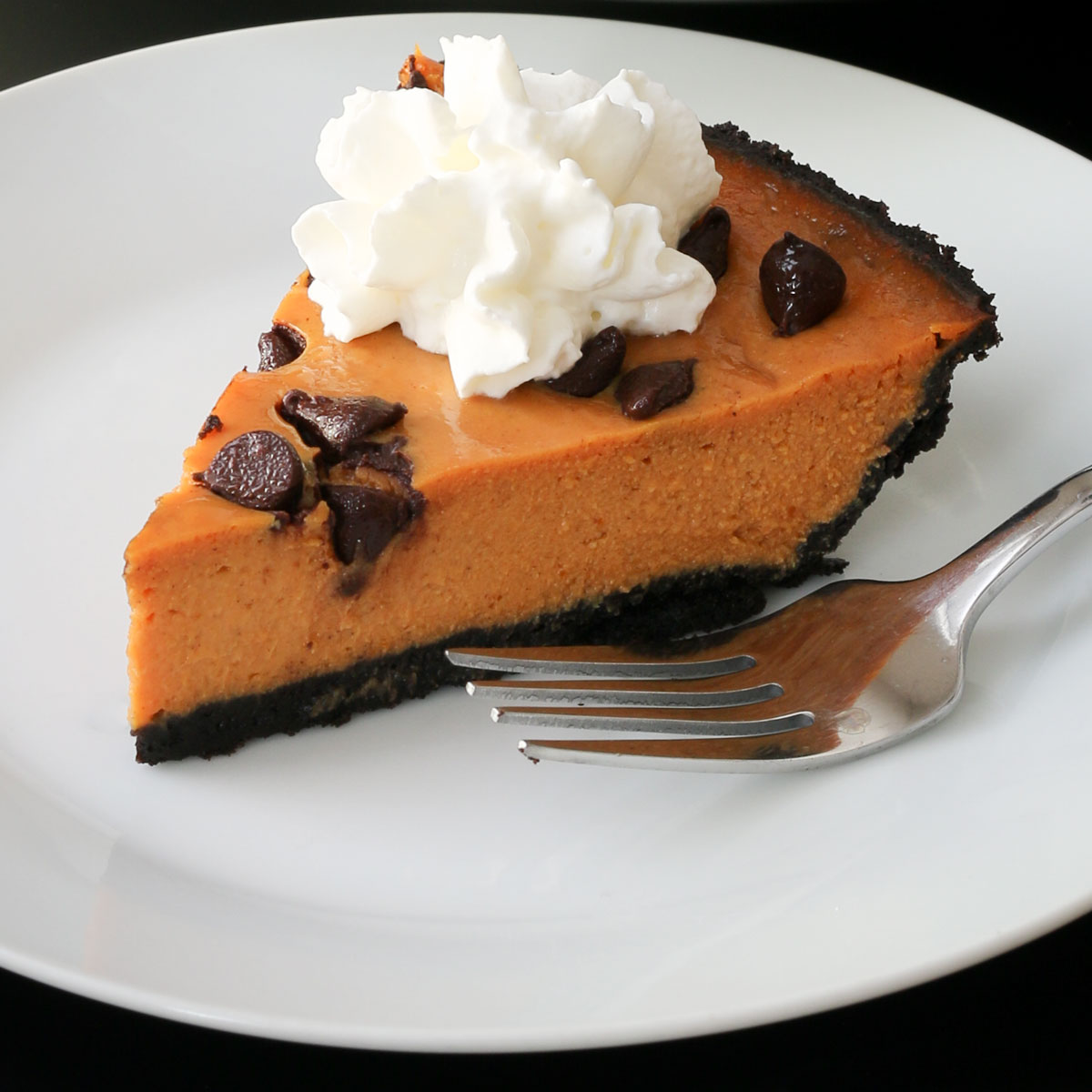 slice of pumpkin pie with chocolate chips and whipped cream on a white plate with a fork.