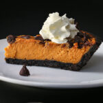 sideview of a slice of pumpkin pie with chocolate on a white plate with whipped cream on top.