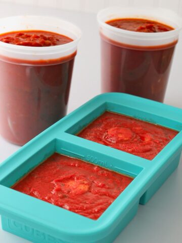 two tubs of spaghetti sauce next to souper cube of sauce.