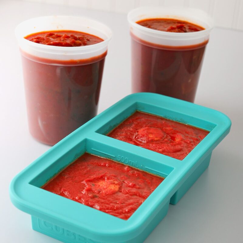 two tubs of spaghetti sauce next to souper cube of sauce.