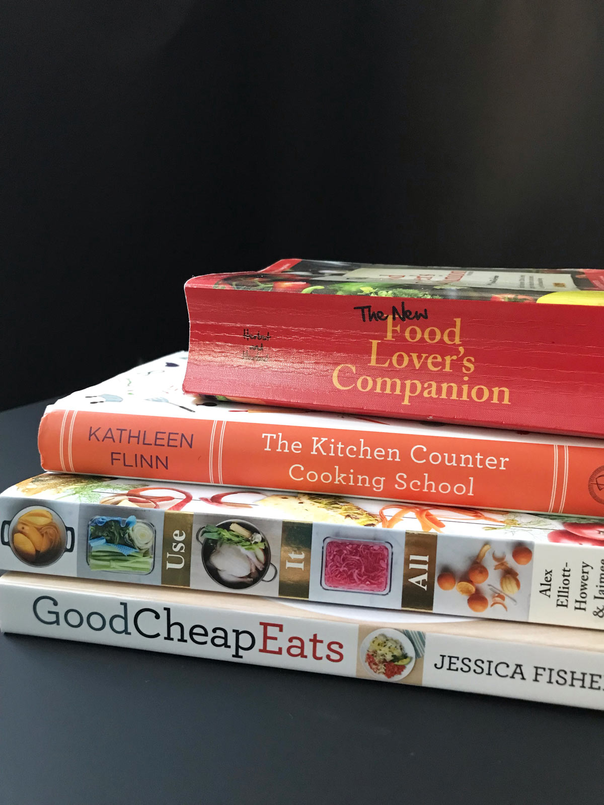 stack of cookbooks and kitchen books on black table.