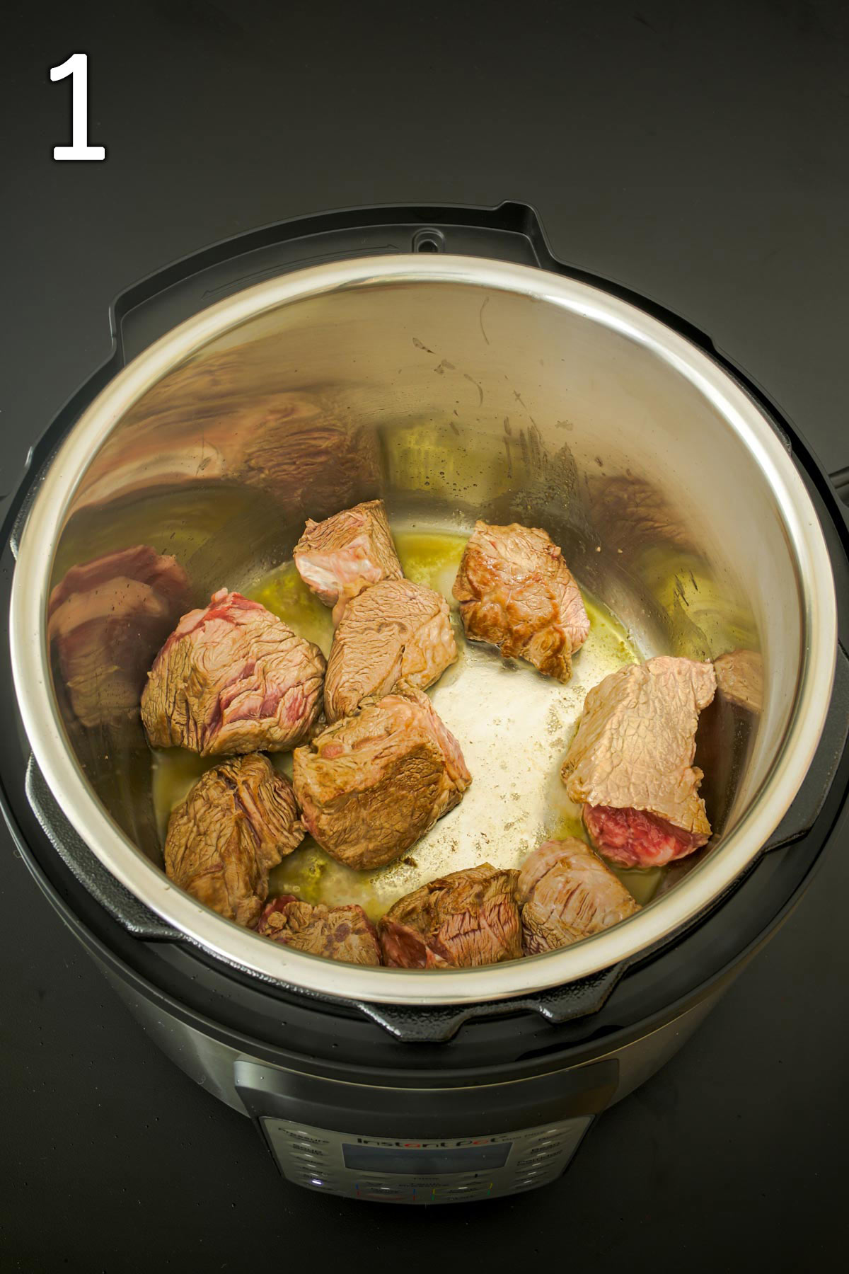beef cubes frying in oil in the metal insert of the instant pot.