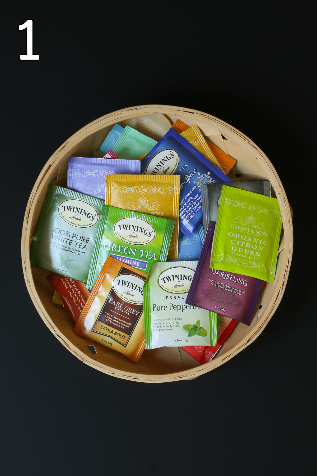 a basket of a selection of different teas in individual packets on a black table.
