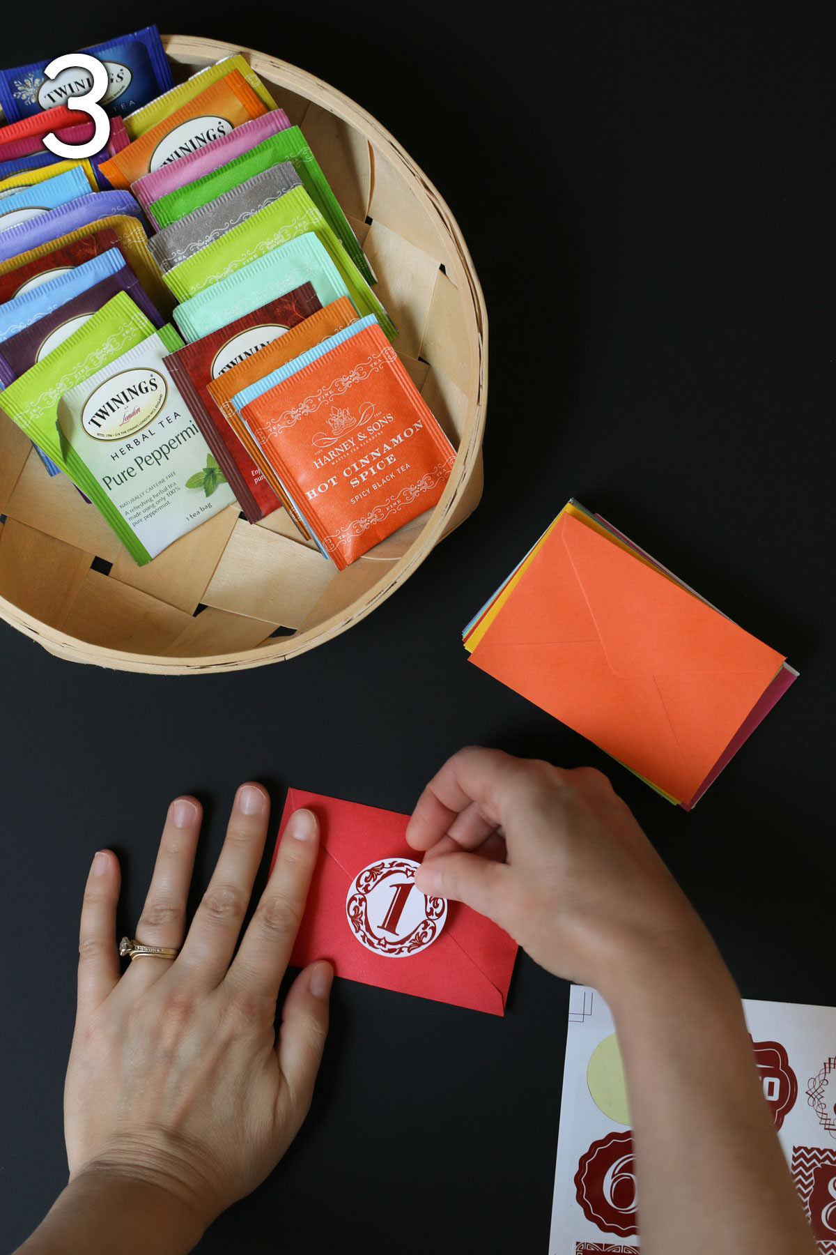 placing a number sticker on the red envelope with the other stickers, envelopes, and tea on the table nearby.