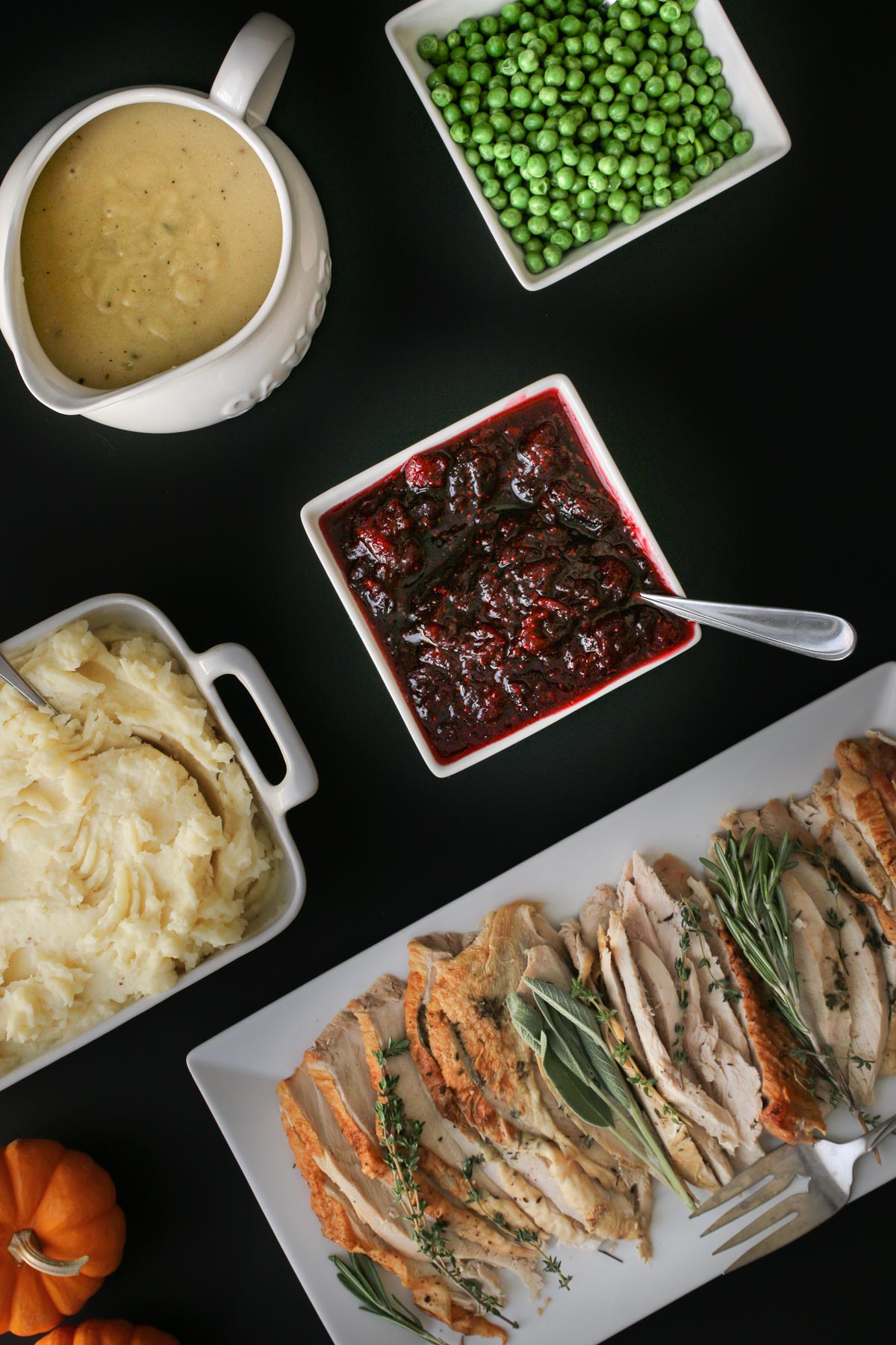 black table set with a number of holiday dishes, including cranberry sauce.