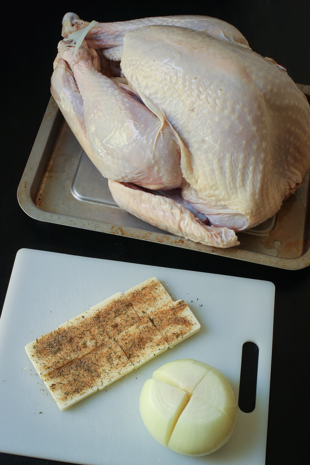 whole uncooked turkey with pats of butter slipped under the skin, the turkey is on a rimmed tray.