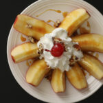 overhead shot of apple slices and caramel with whipped cream, nuts, and a cherry on a white plate.