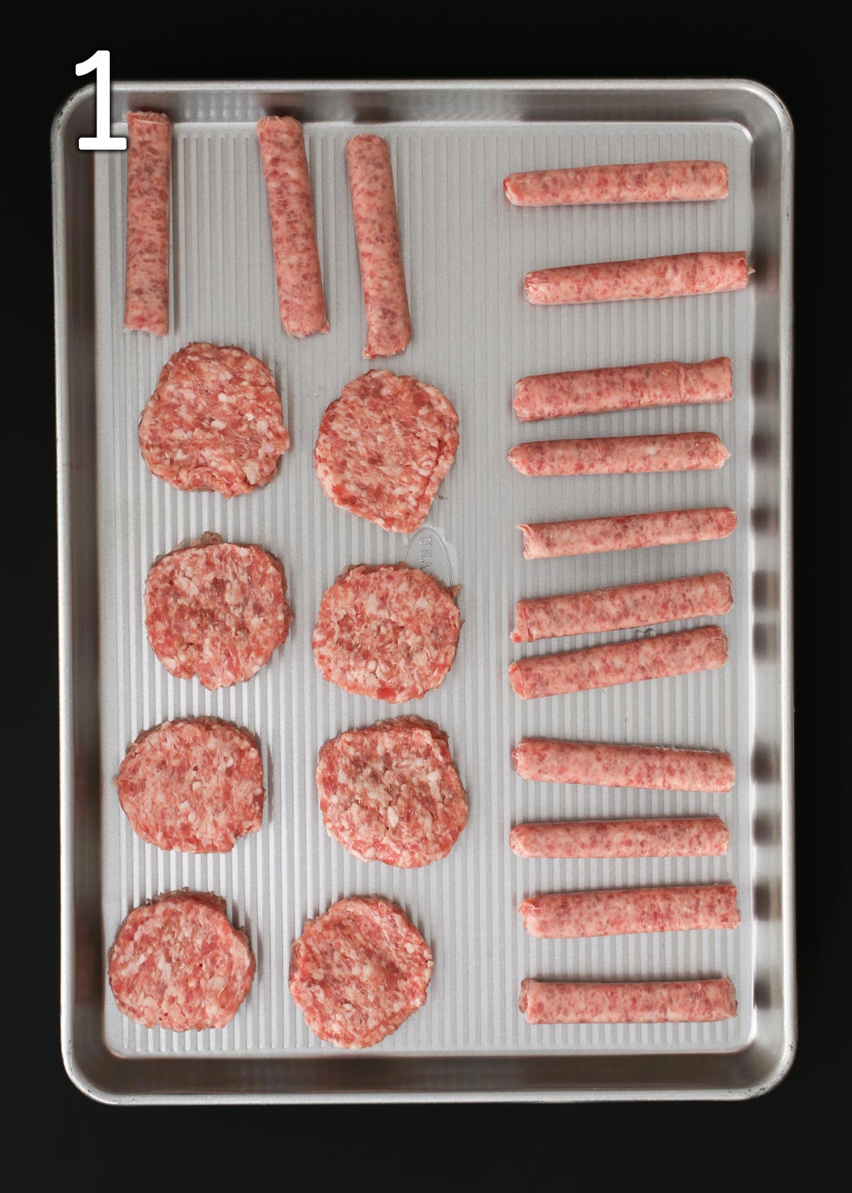 uncooked sausages on rimmed sheet pan on black table.