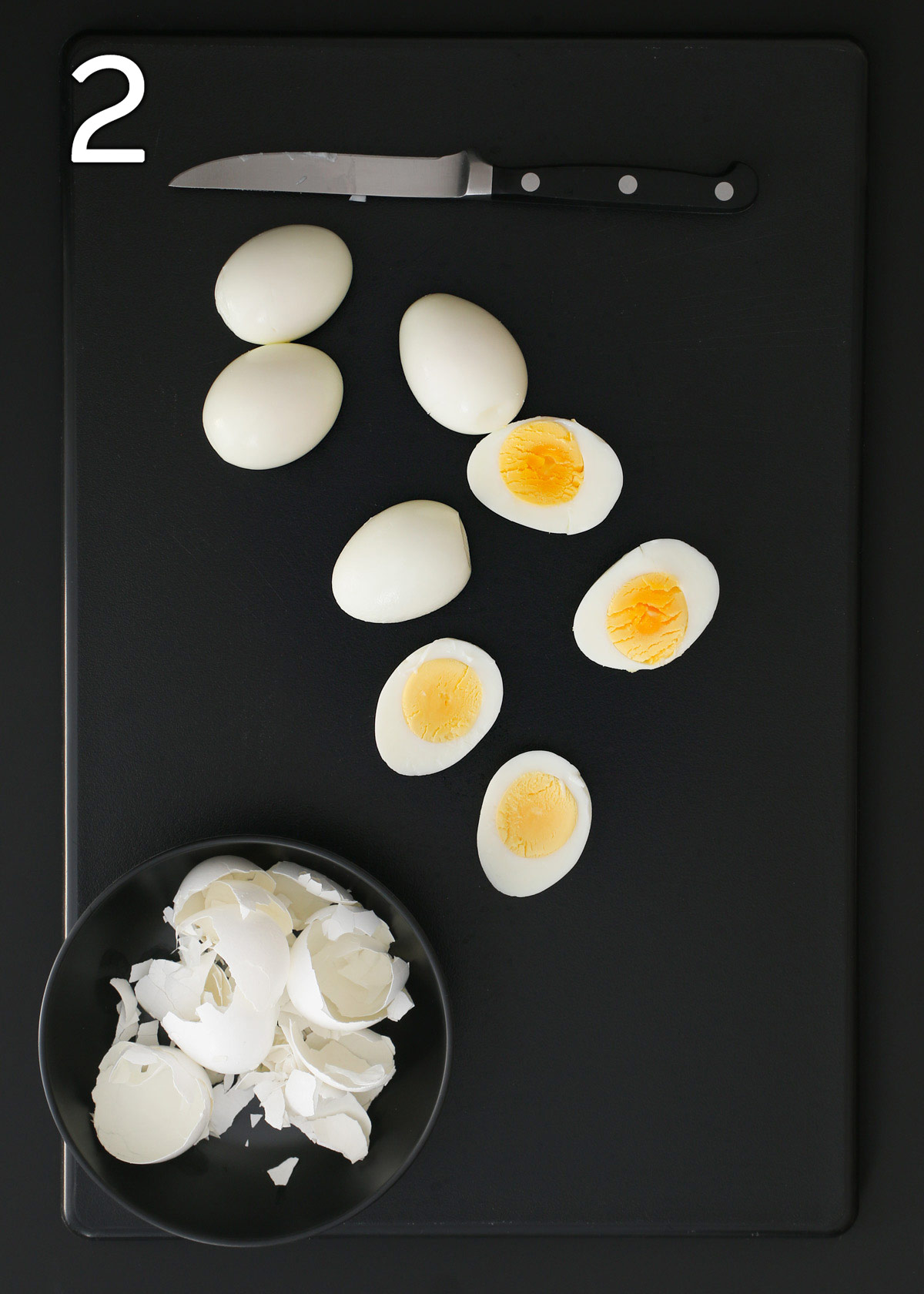 peeled eggs on black cutting board with a knife.