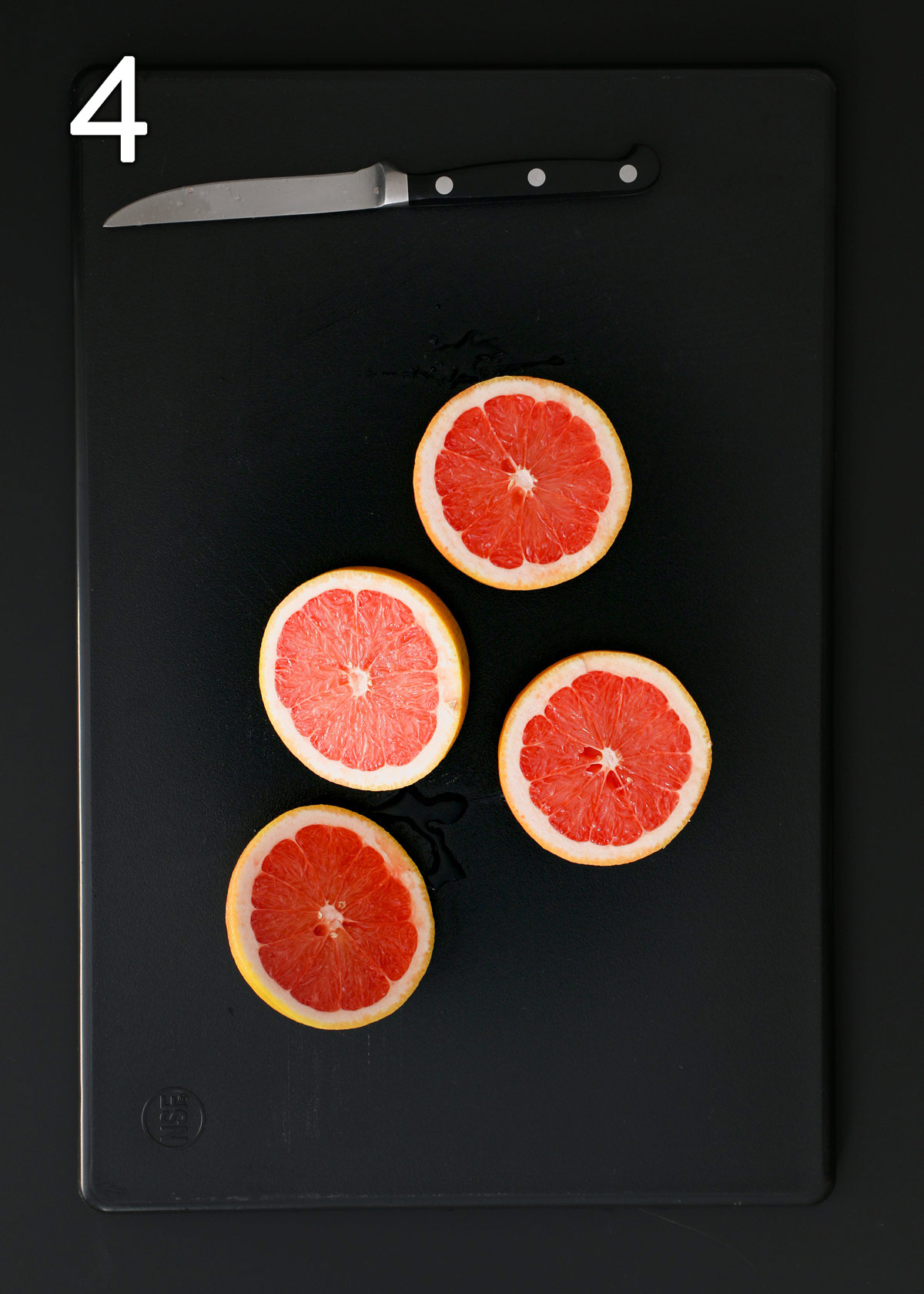 grapefruit cut in half on a black cutting board with a knife.