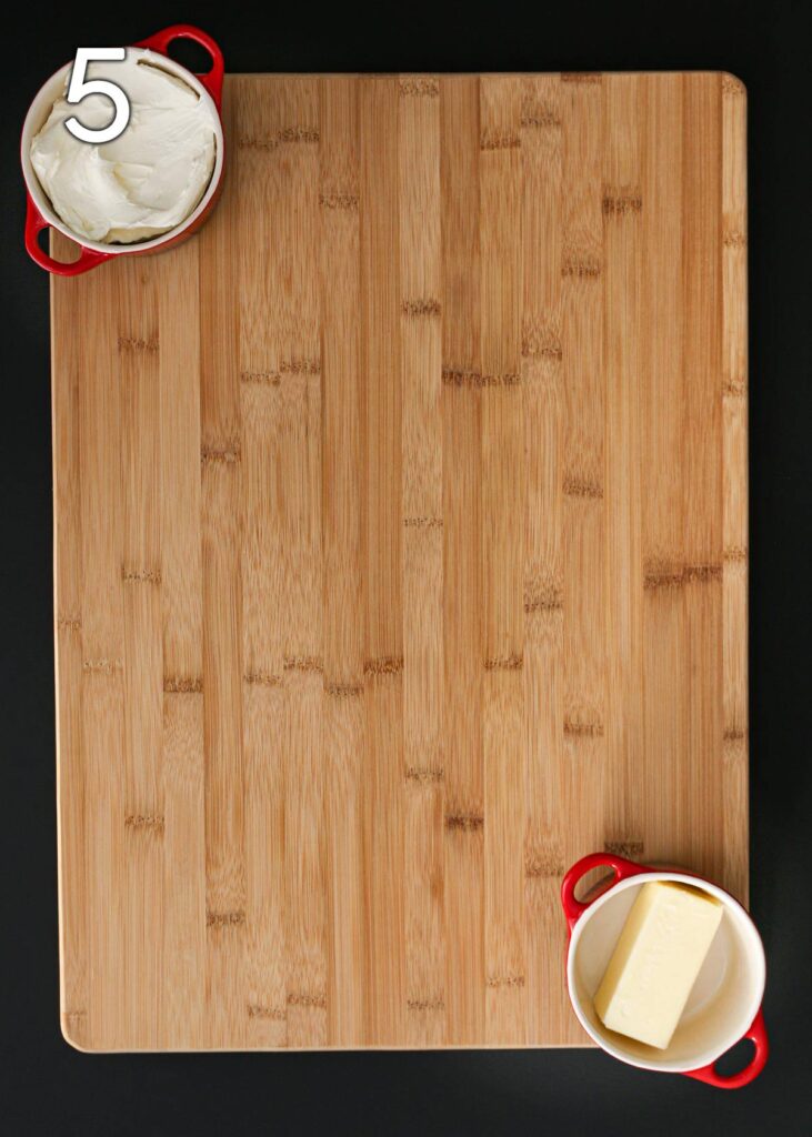 cream cheese and butter dishes on wooden cutting board.