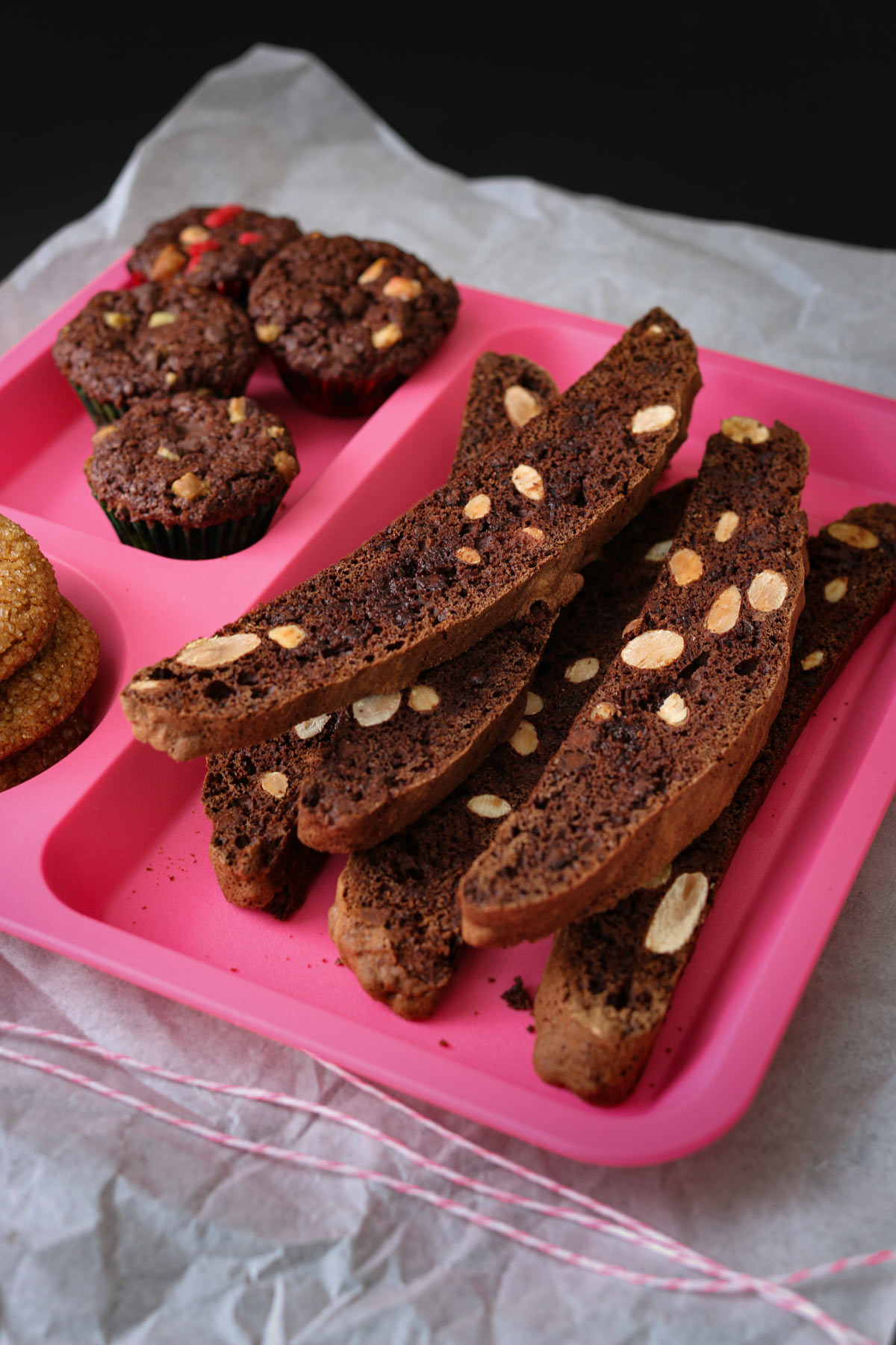 pink divided tray filled with biscotti, brownie bites, and molasses cookies on a piece of parchment.