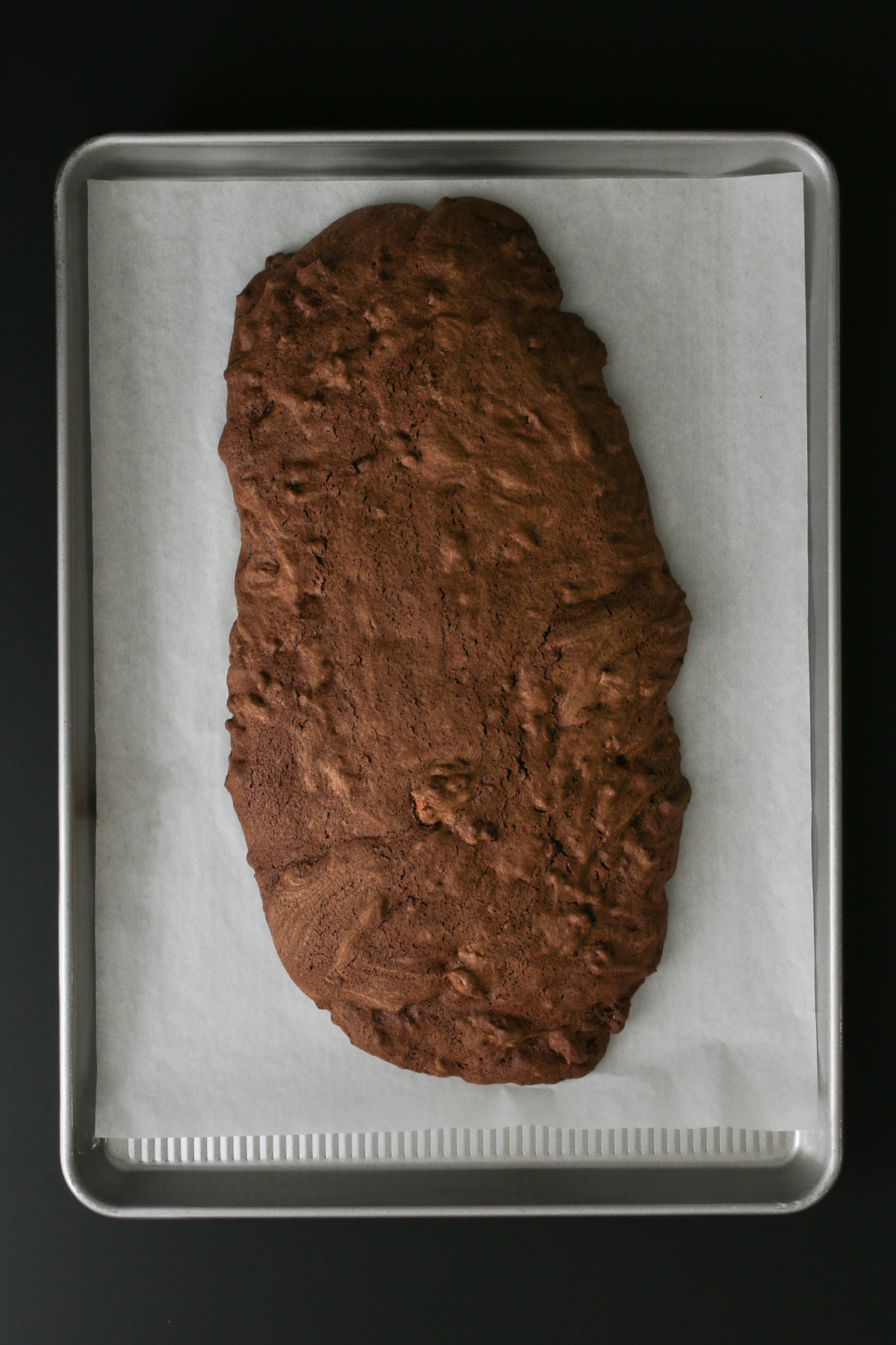 the baked log of chocolate biscotti batter down the center of the parchment paper.